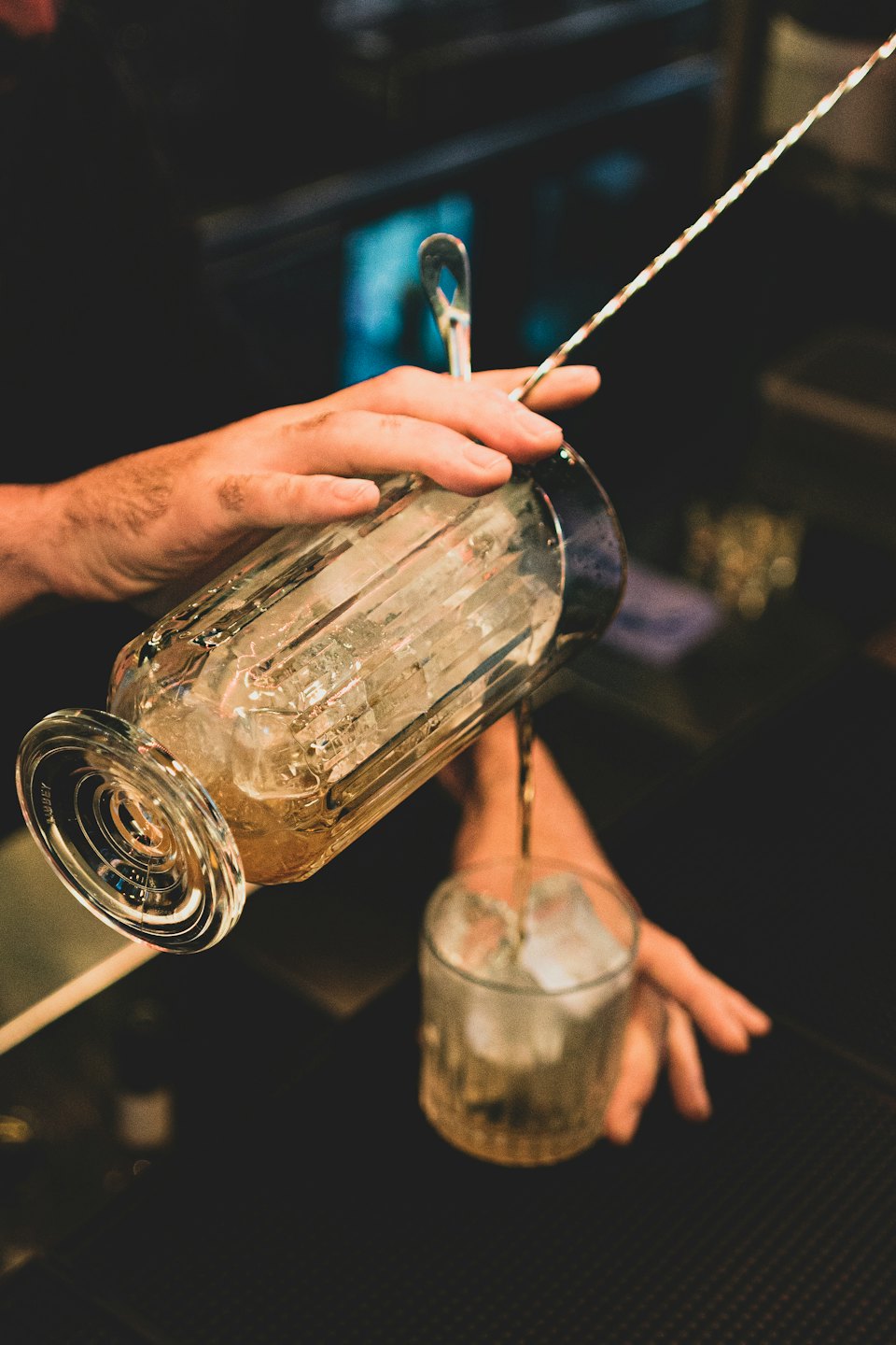 Un camarero sirve un cóctel colorido en un vaso bajo con hielo.