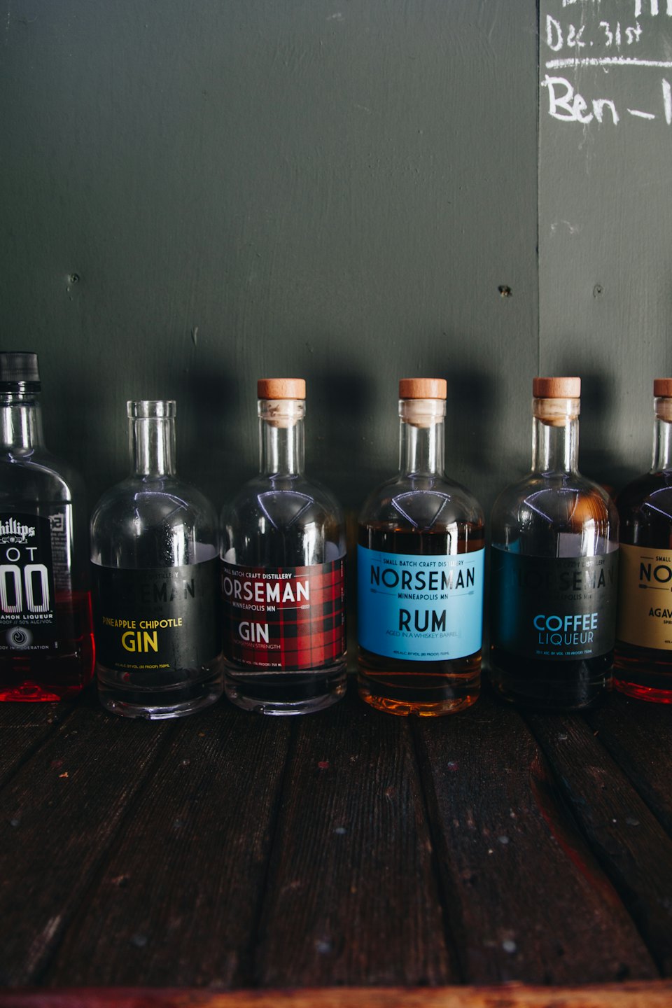 Siete botellas de licor de vidrio en fila sobre un mostrador de madera.